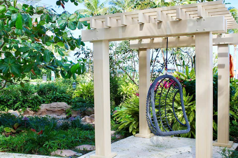 White pergola with hanging bicycle wheel decoration in lush tropical garden setting