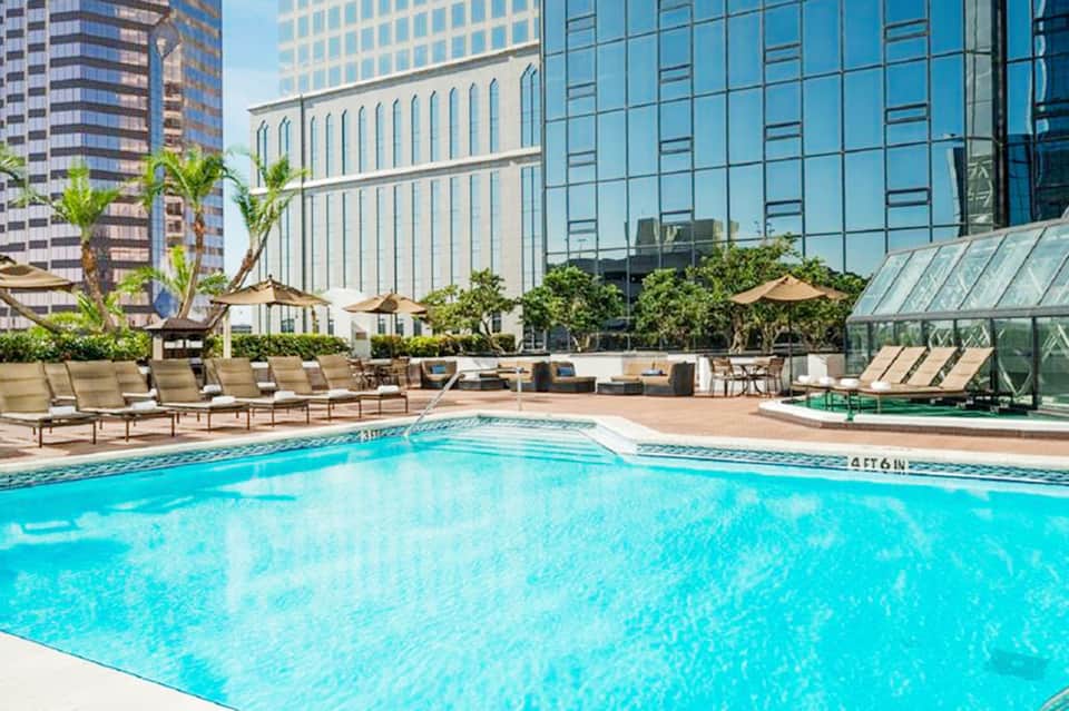 Resort pool surrounded by lounge chairs, tall buildings, and umbrellas in urban setting