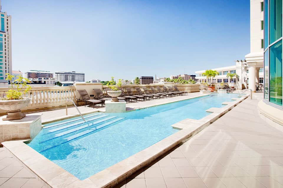 Rectangular rooftop pool with lounge chairs and city skyline views on a clear day