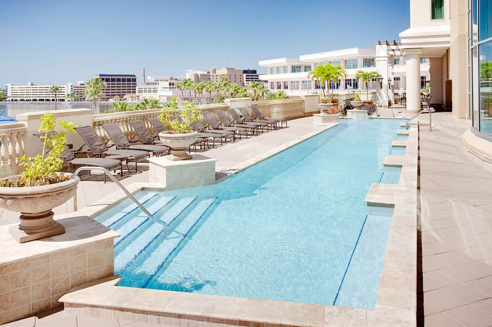 Rooftop infinity pool with lounge chairs overlooking urban cityscape and classical balustrade railings