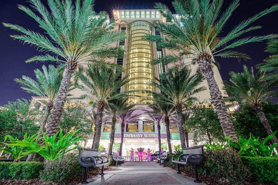 Embassy Suites hotel entrance at night, illuminated with palm trees lining the courtyard