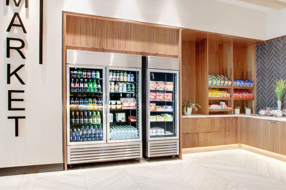 Modern market area with wooden cabinetry, refrigerated beverage displays, and shelving with snacks and products
