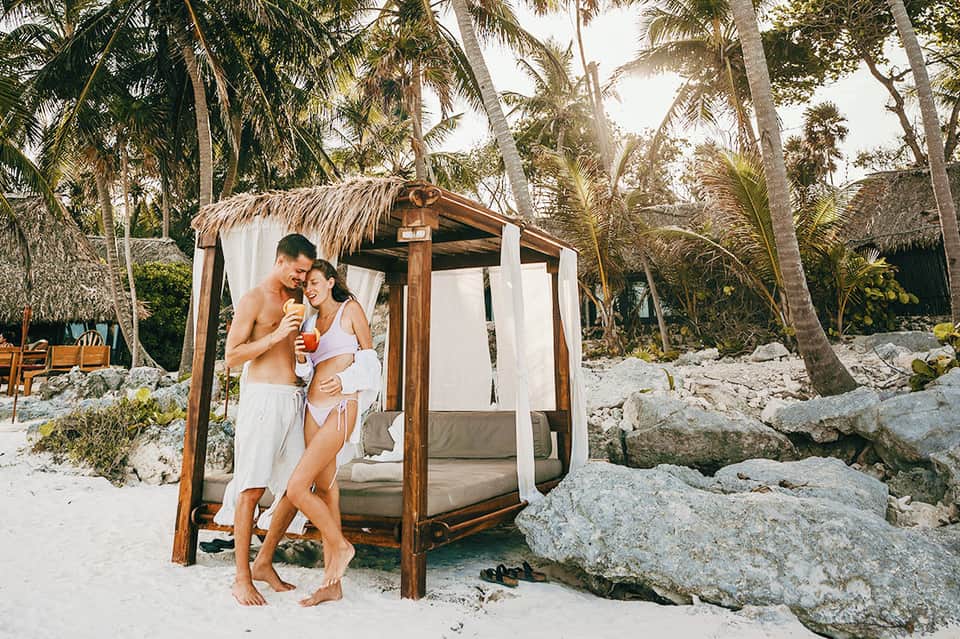 Couple relaxing in beachfront cabana with palm trees and sandy beach