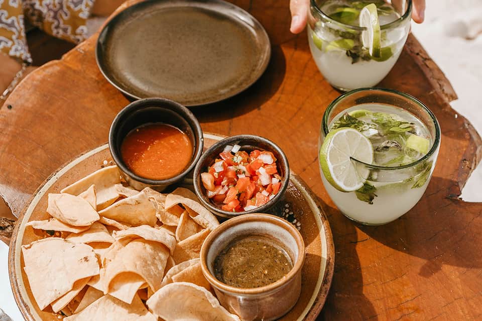 Overhead view of Mexican appetizers with tortilla chips, salsas, guacamole, and lime mojito cocktails