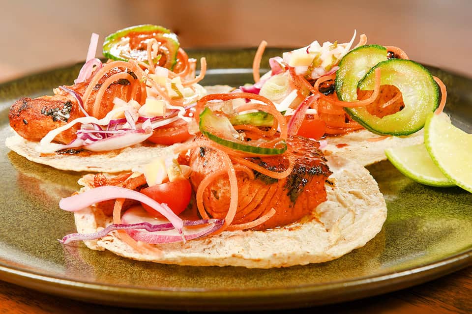 Grilled meat tacos with fresh vegetables, onions, and jalapeños served on a plate