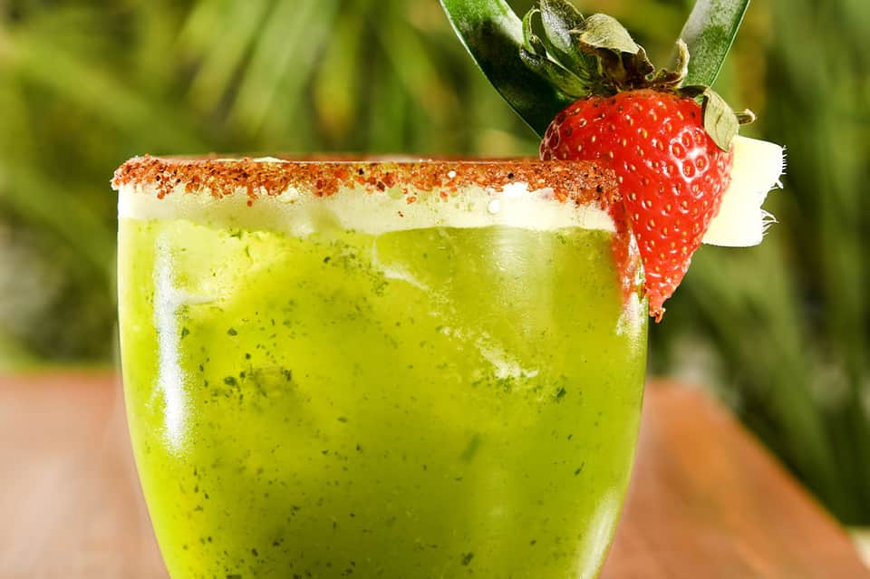 Vibrant green cocktail with cinnamon sugar rim and fresh strawberry garnish against blurred garden background