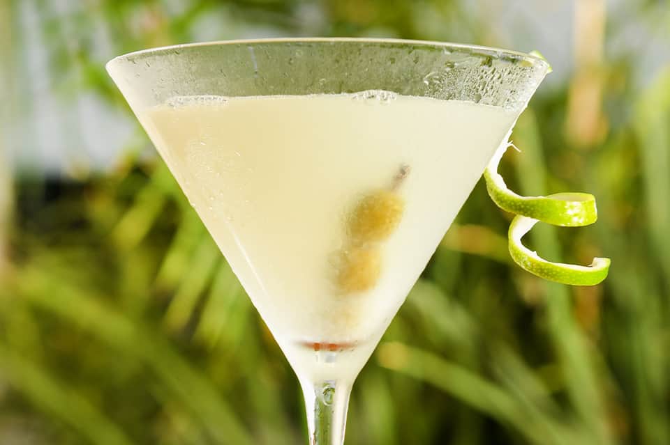Elegant martini cocktail with olive garnish and lime twist on blurred garden background