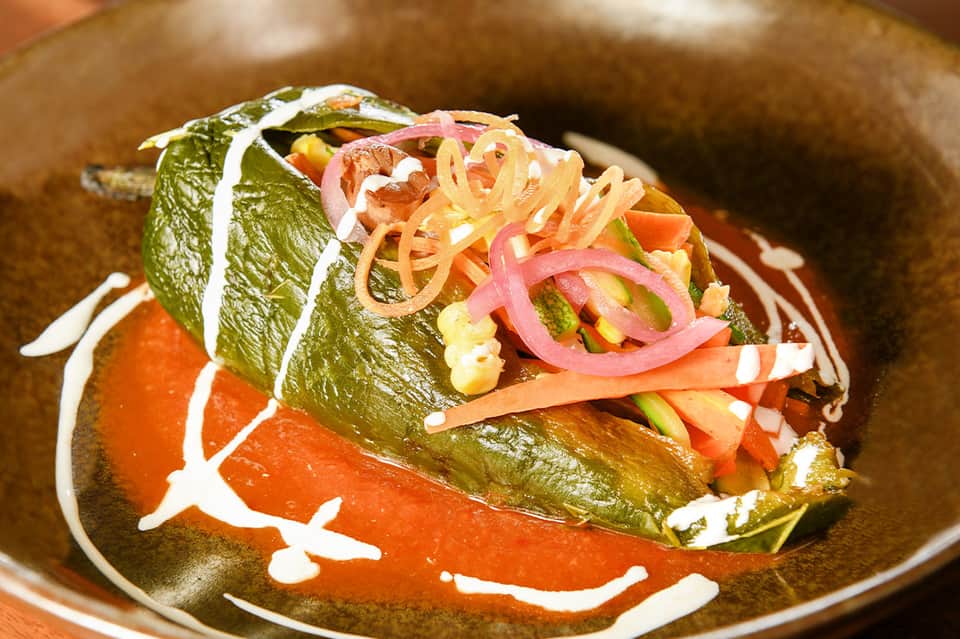 Gourmet appetizer with green leaf wrap, pickled ginger, and sriracha on ceramic plate