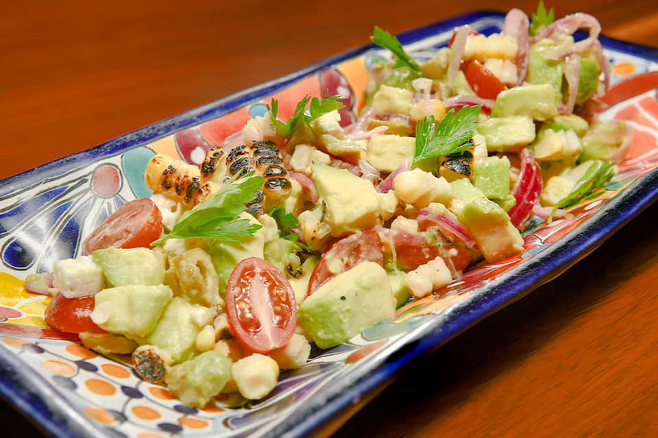 Plated salad with grilled shrimp, avocado, tomato, and fresh herbs on decorative ceramic plate