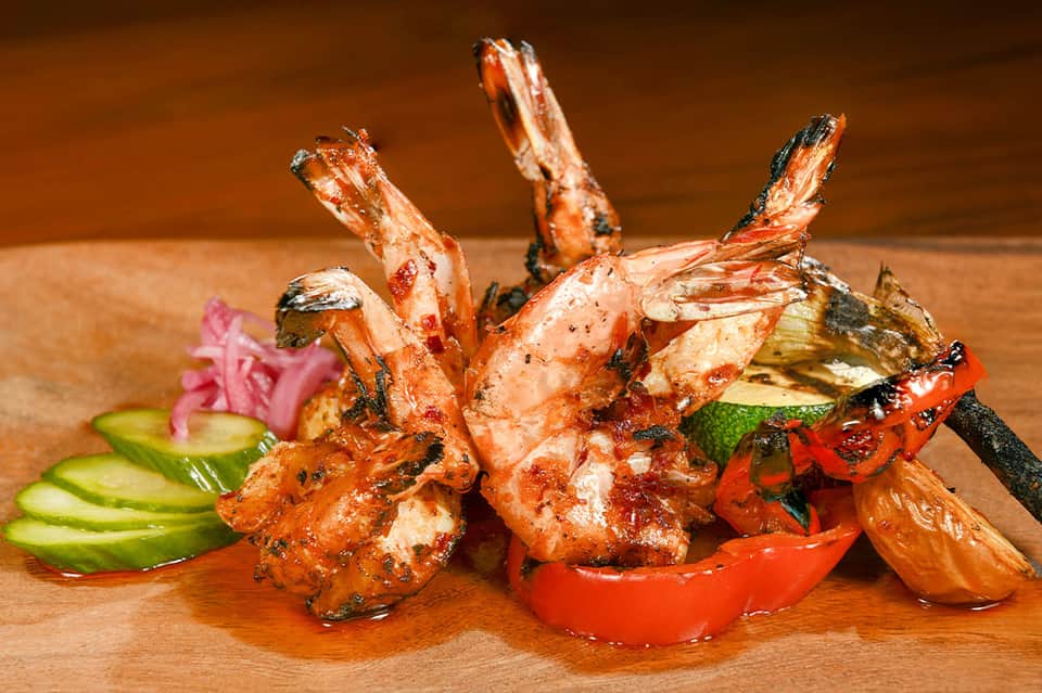 Grilled shrimp skewers with vegetables and pink pickled ginger on wooden serving board