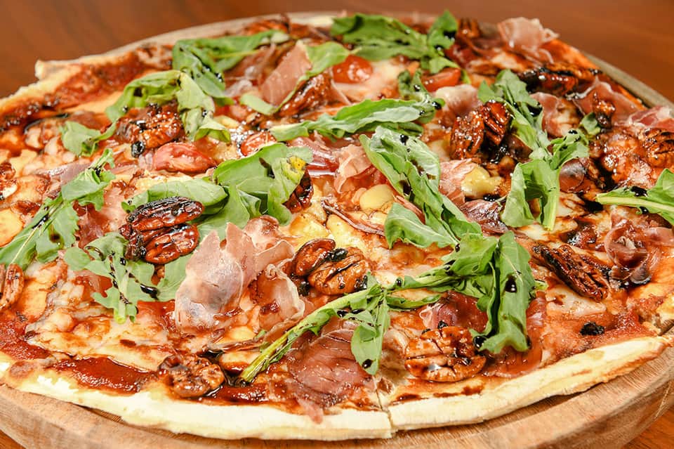 Gourmet pizza topped with prosciutto, caramelized onions, arugula, and fresh herbs on wooden board