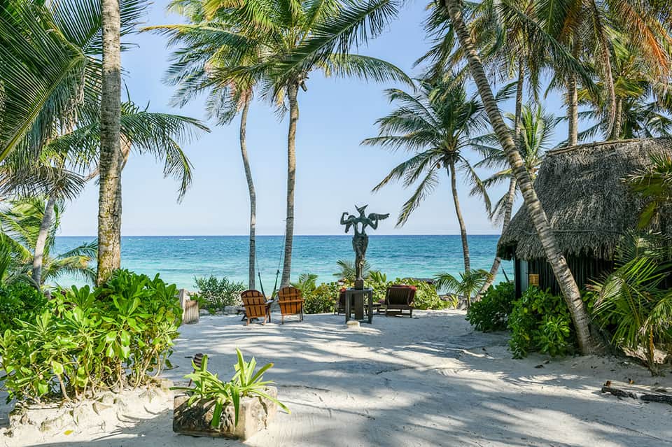 Tropical beach with palm trees, wooden lounge chairs, and thatched-roof structures