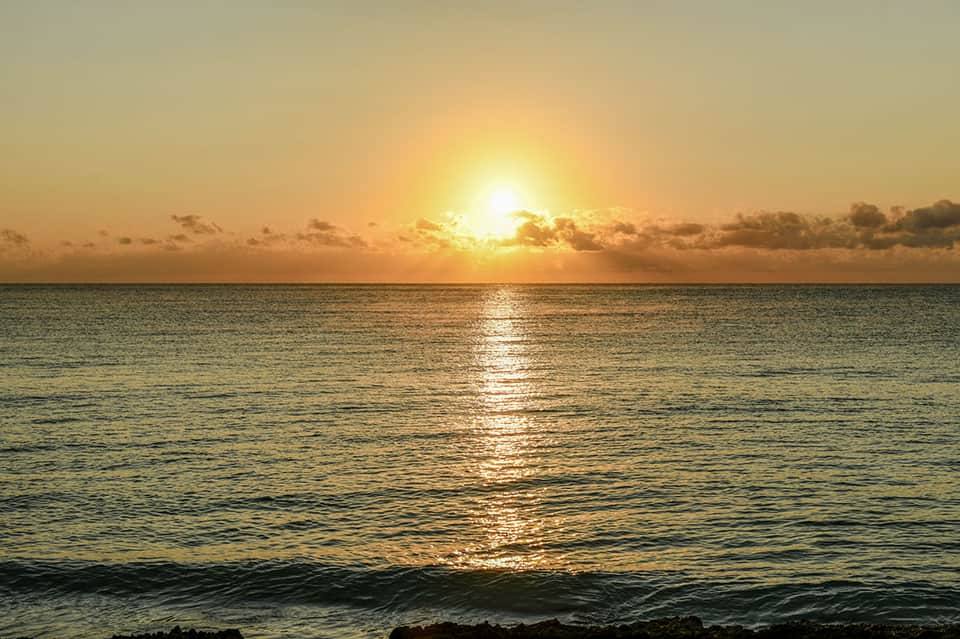 Golden sunset over calm ocean waters with clouds and sun reflecting on the sea