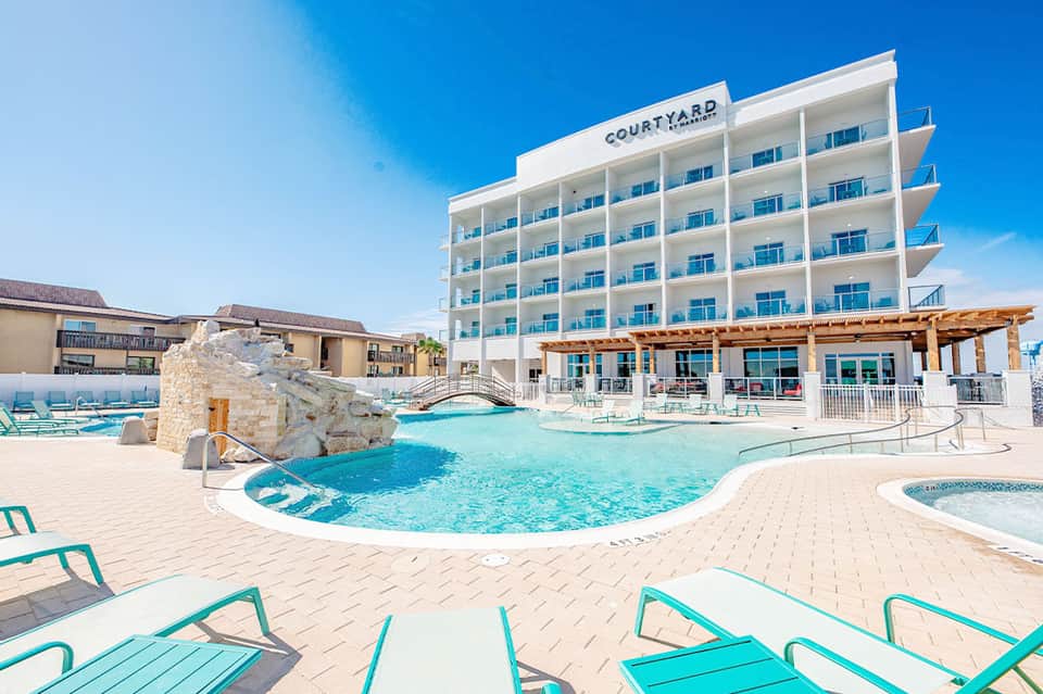 Beachfront resort pool with turquoise water, white modern hotel building, and lounge chairs under clear blue sky