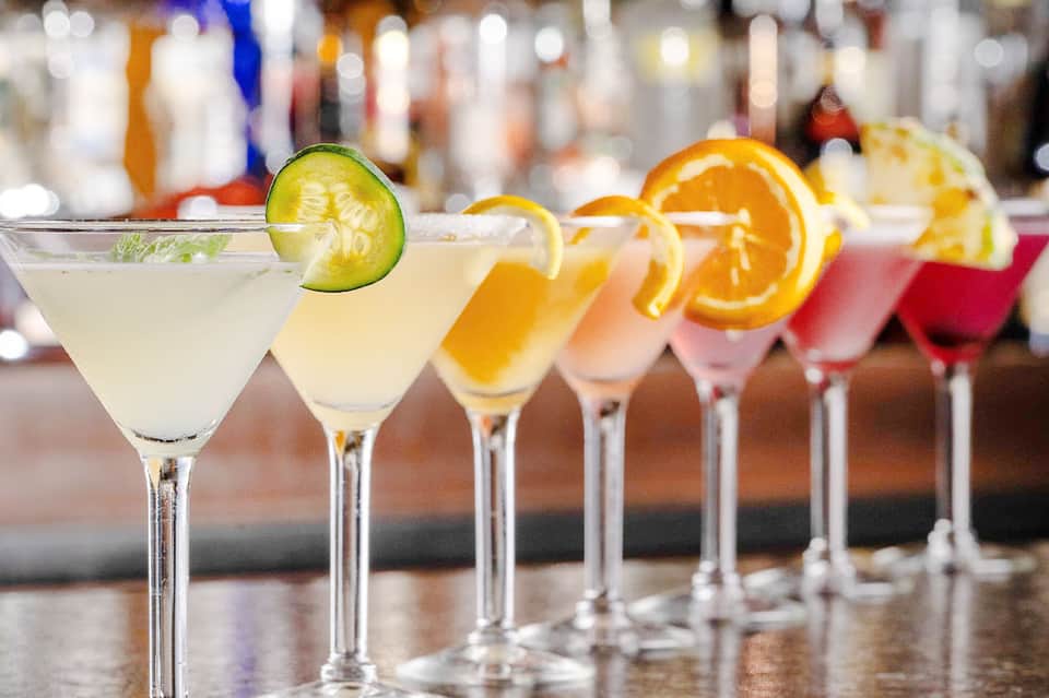 Colorful cocktails lined up at bar with citrus garnishes and lime slices