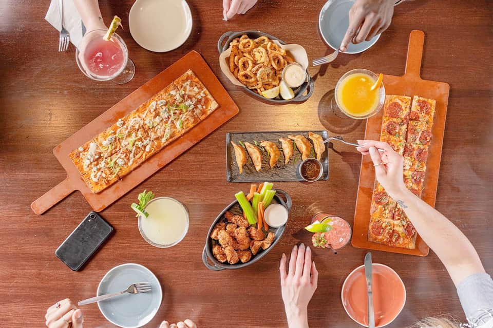 Overhead view of shared dining table with pizza, appetizers, and beverages