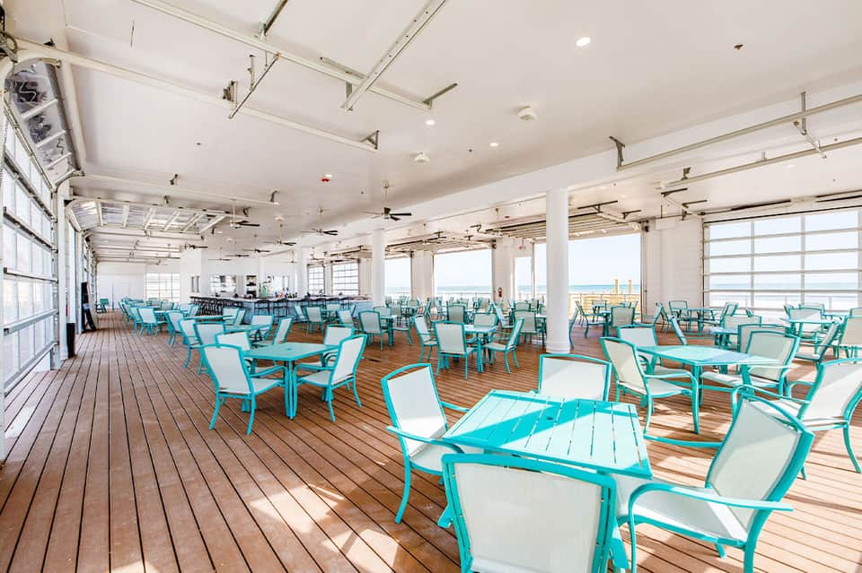 Spacious covered deck with turquoise lounge chairs, white columns, and ocean horizon views