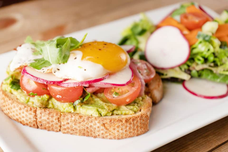 Avocado toast with poached egg, tomato, and radish on whole grain bread with side salad