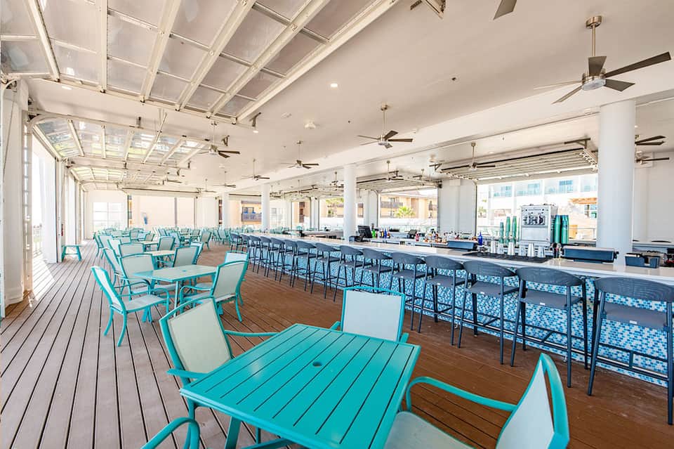 Modern rooftop dining area with turquoise and black chairs, wood decking, and glass skylights overhead