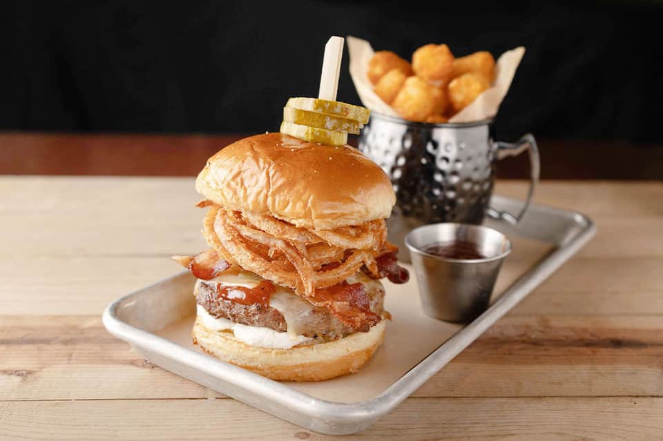 Gourmet burger with crispy onion strings, bacon, and fries on wooden serving board