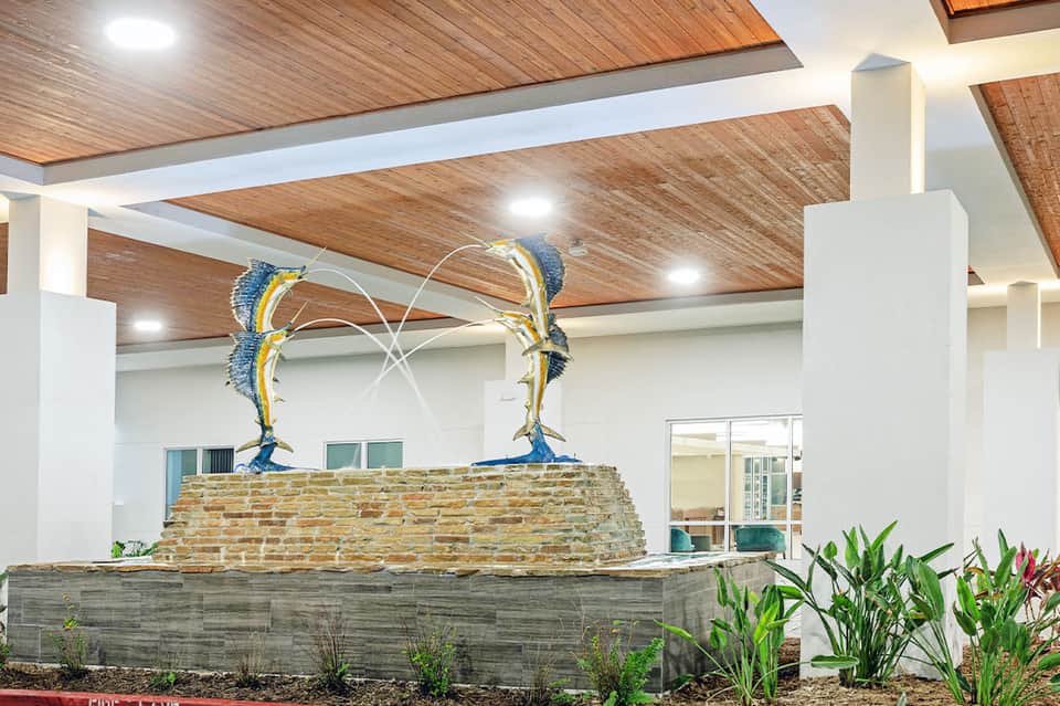 Modern lobby entrance with two blue marlin sculptures mounted on stone base, wood ceiling, and tropical plants