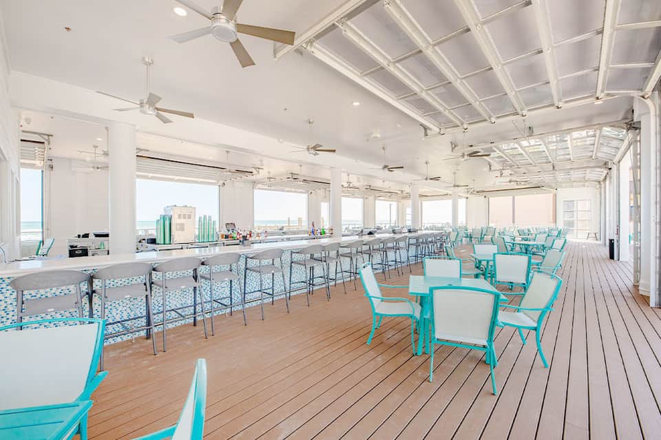 Modern covered deck bar with turquoise chairs, wooden flooring, and ocean views