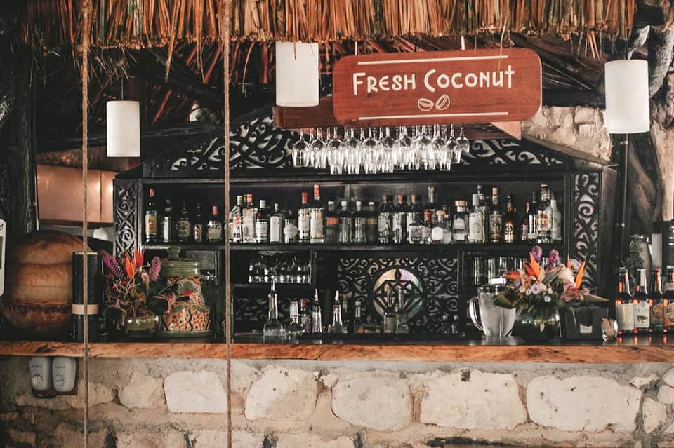 Tropical tiki bar with fresh coconut drink sign, stocked shelves, and decorative elements