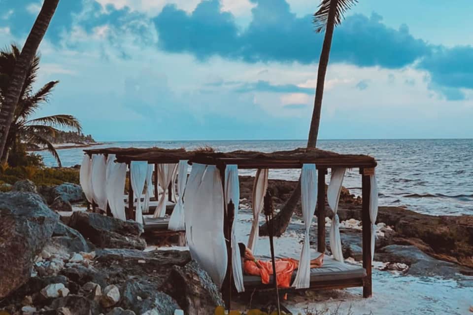 Rustic beachfront cabana with flowing white curtains and ocean backdrop at dusk