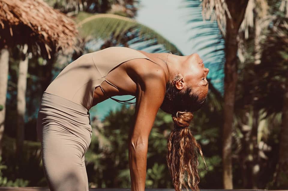 Woman performing backbend yoga pose between palm trees in tropical setting
