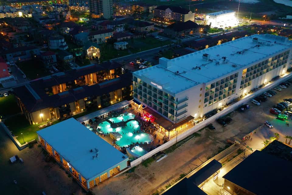 Aerial night view of illuminated resort with glowing pool deck and courtyard surrounded by buildings