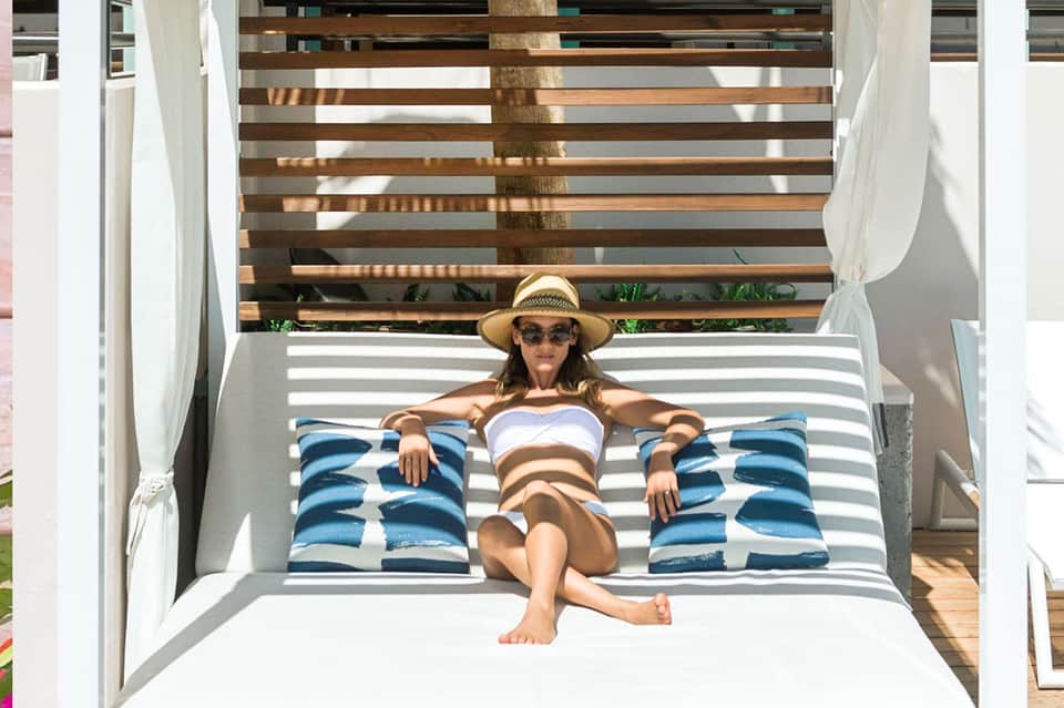 Woman relaxing on striped lounge chair with blue pillows and straw hat on sunny patio