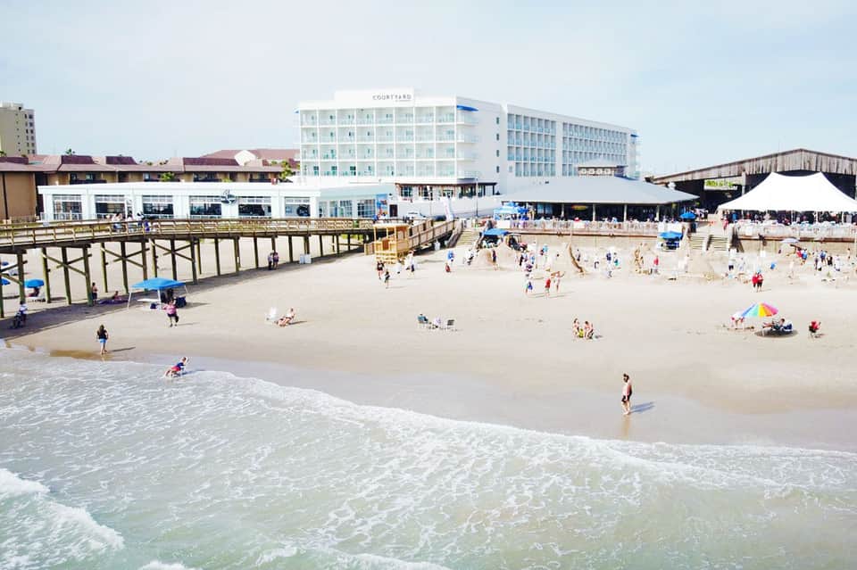 Sandy beach with Courtyard hotel, pier, and crowds of beachgoers on sunny day