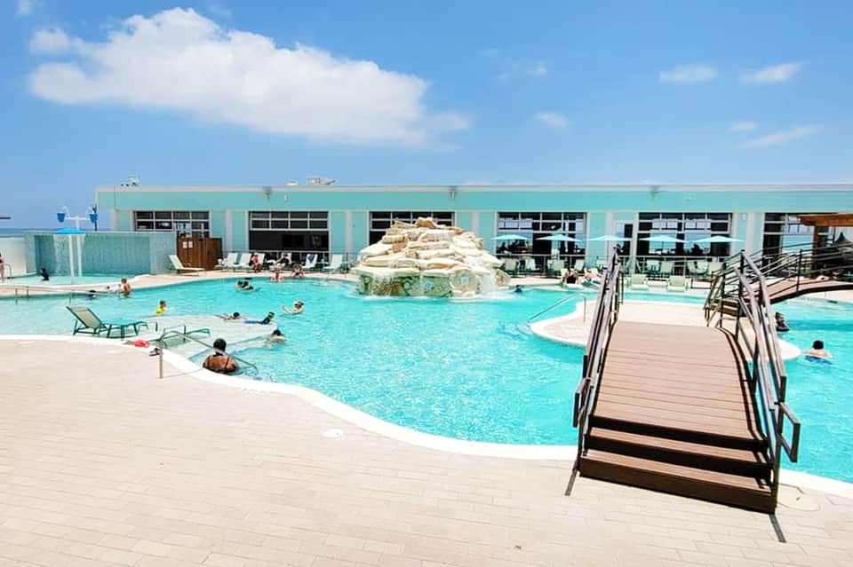 Outdoor resort pool with turquoise water, white loungers, and turquoise building backdrop