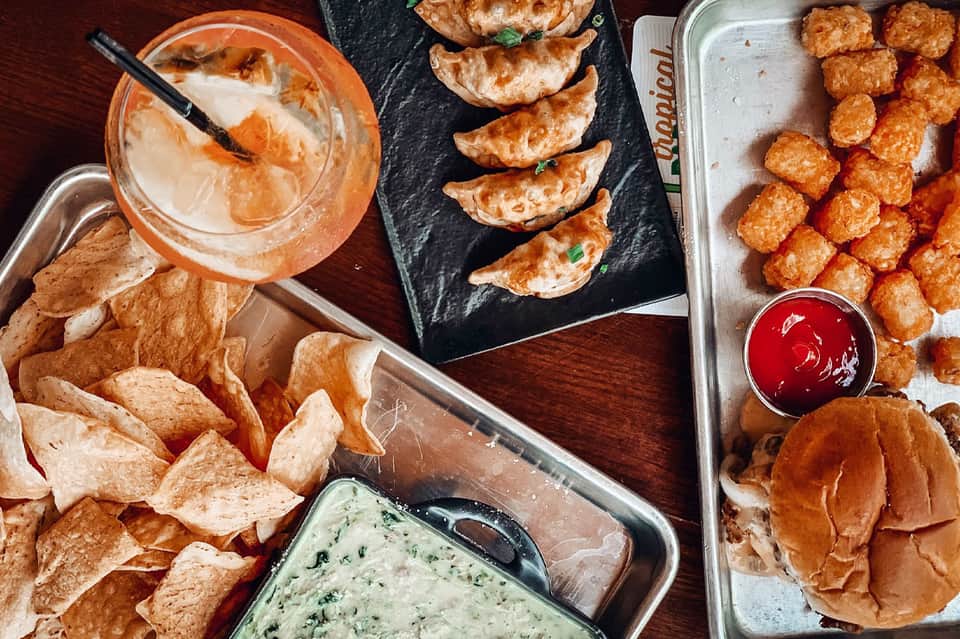 Appetizer spread featuring chips with dip, dumplings, fried appetizers, and cocktail on wooden table