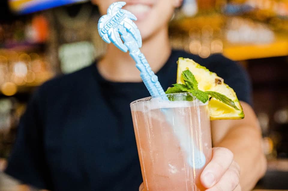 Tropical cocktail with blue decorative stirrer, pineapple wedge, and mint garnish in a clear glass
