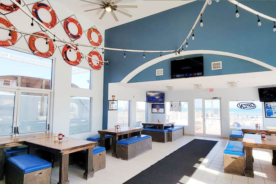 Beachfront restaurant interior with blue curved walls, decorative life rings, and ocean views