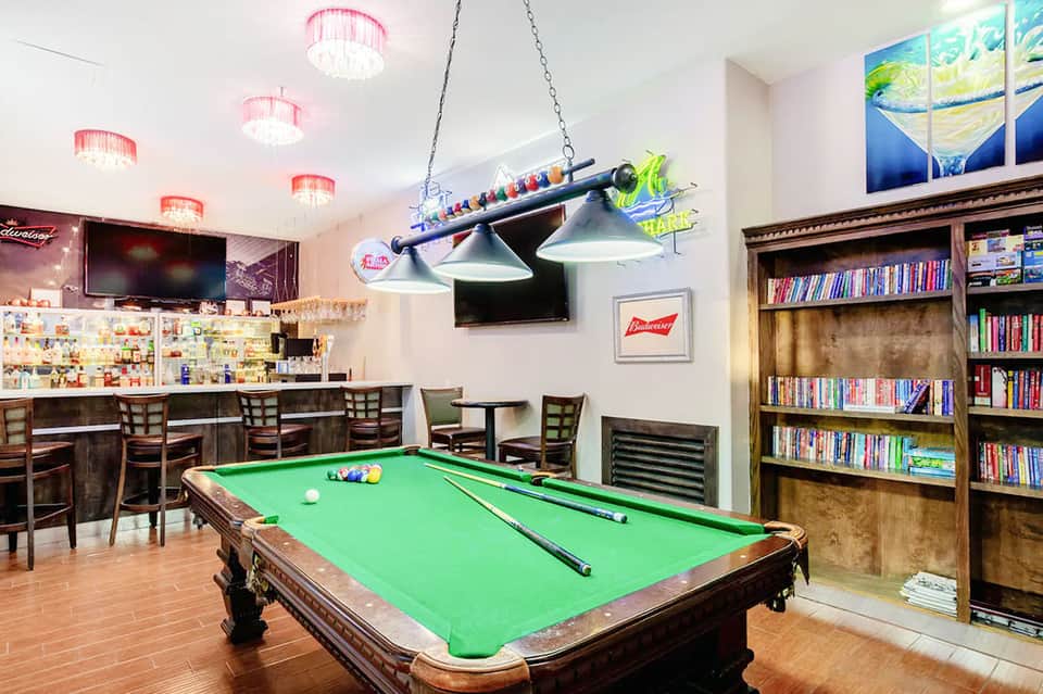 Game room with pool table, bar area, pink ceiling lights, and bookshelves in background