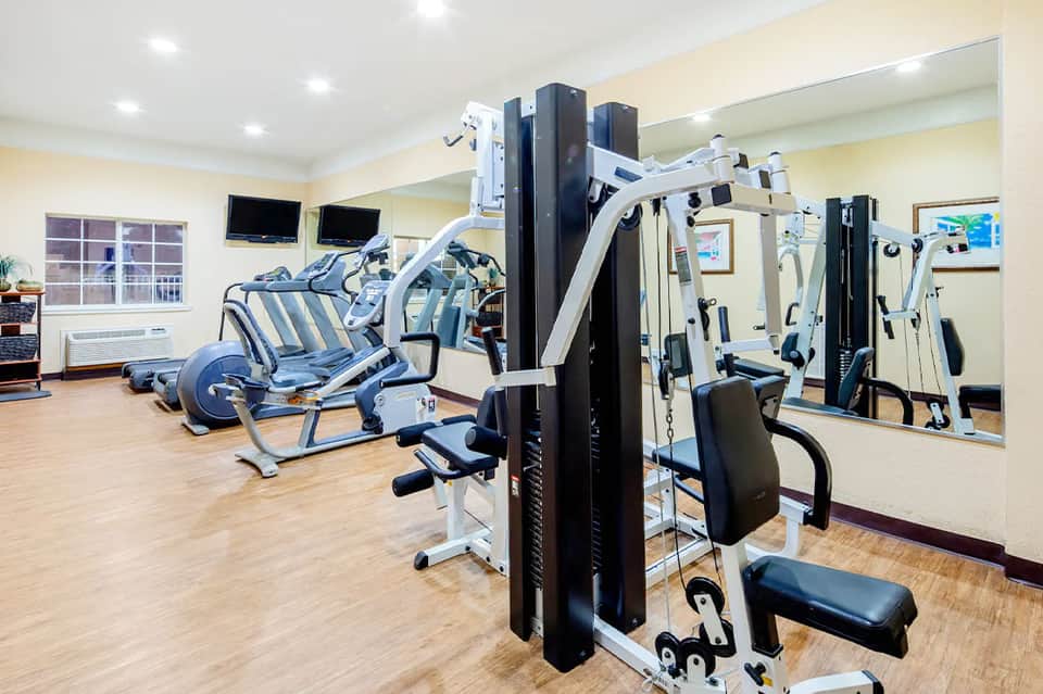 Fitness center with white exercise machines, cardio equipment, and wooden flooring