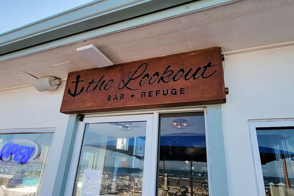 Wooden 'The Lookout Bar + Refuge' sign on beachfront establishment entrance