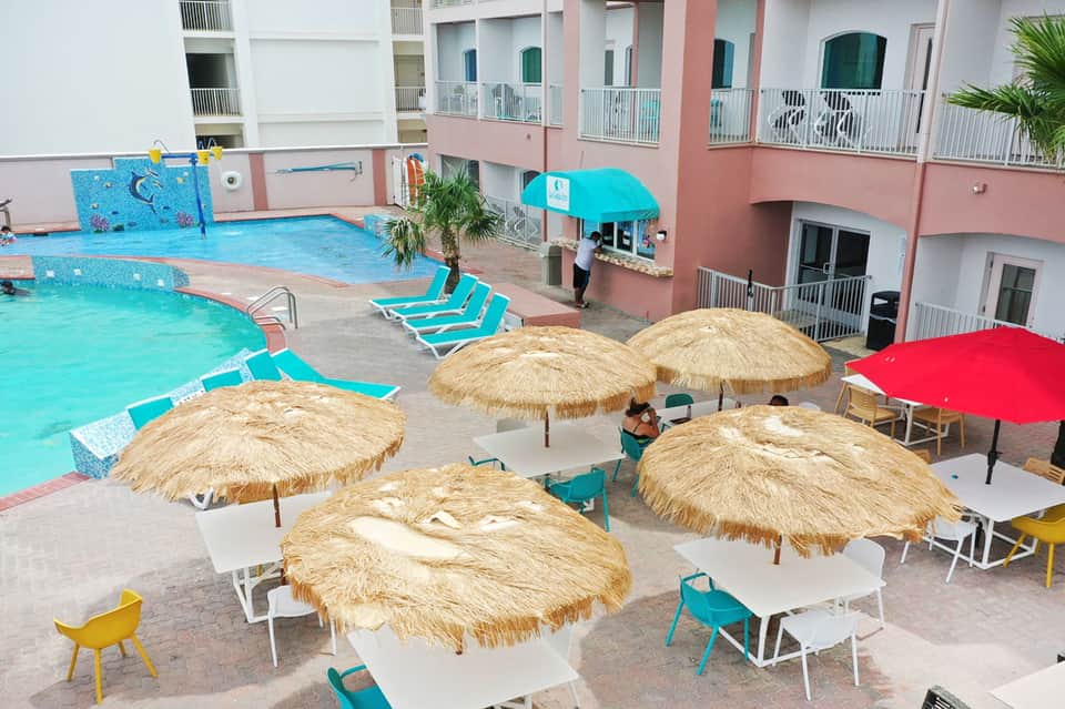 Resort pool area with thatched umbrellas, colorful loungers, and pink building complex