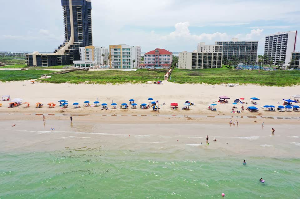 Beach scene with colorful umbrellas and beachgoers along sandy shore lined with high-rise hotels