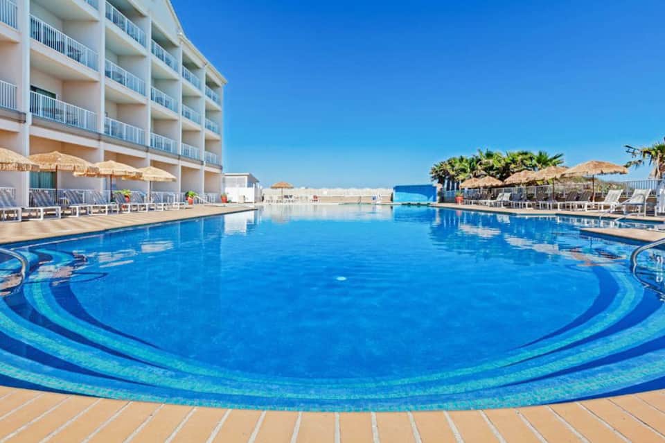Resort pool with decorative beach balls and white lounge chairs along the waterfront