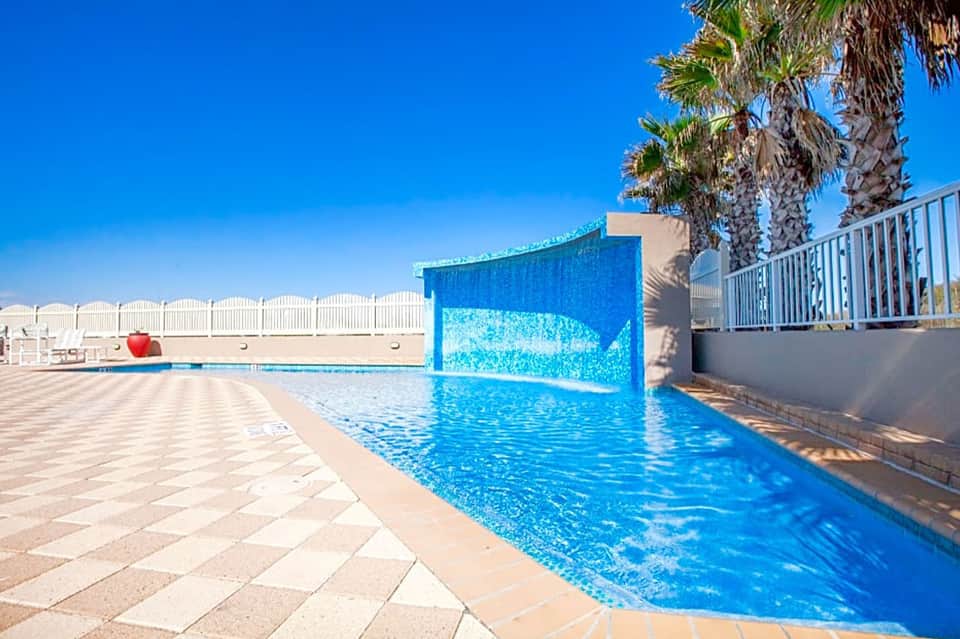 Resort swimming pool with blue water and modern architectural waterfall feature under clear sky