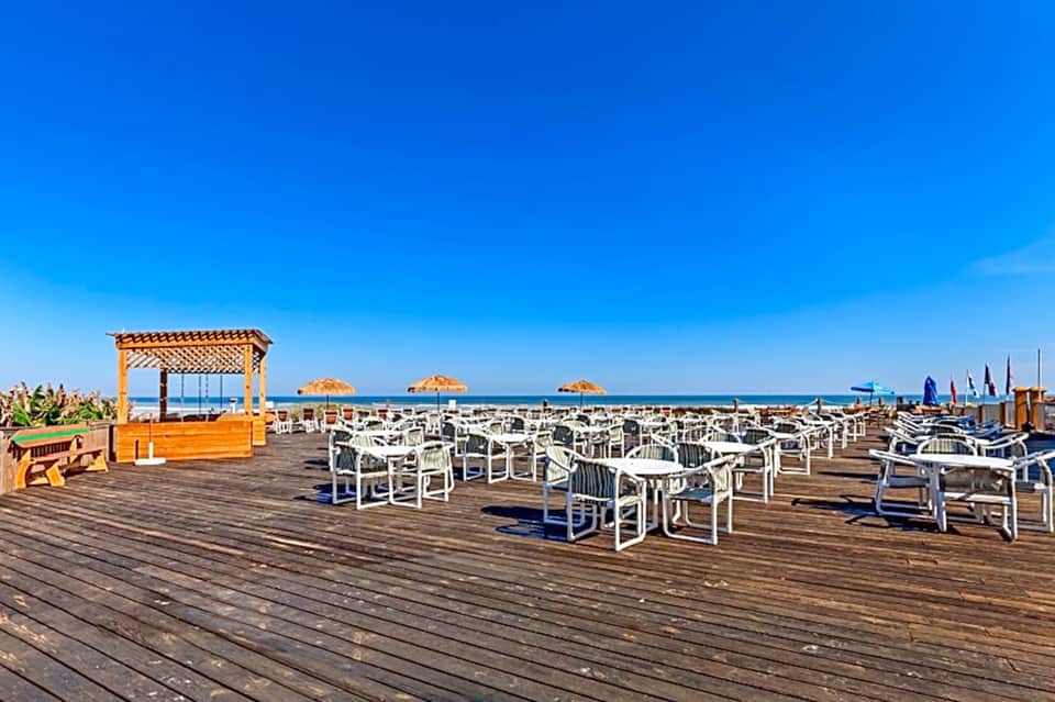 Wooden boardwalk with white chairs and thatched umbrellas overlooking beach and ocean