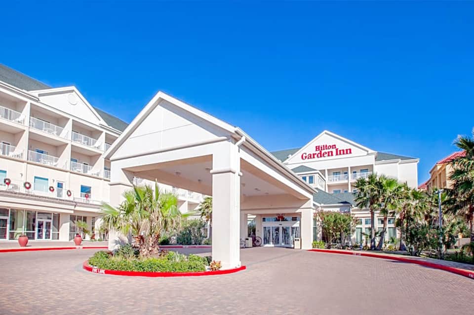 Hilton Garden Inn entrance with white columns, palm trees, and brick paved courtyard