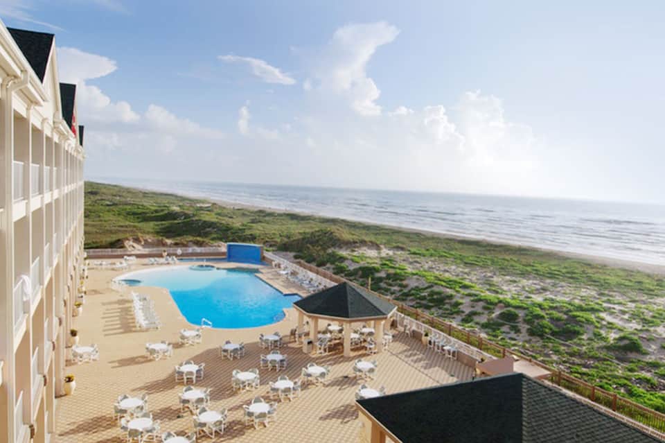 Beachfront resort pool with cabanas overlooking dunes and ocean coastline