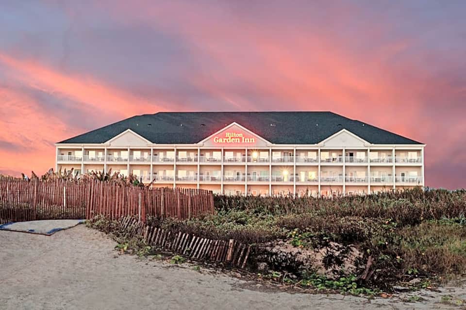 Hilton Garden Inn beachfront hotel at sunset with dune fencing and dramatic pink sky