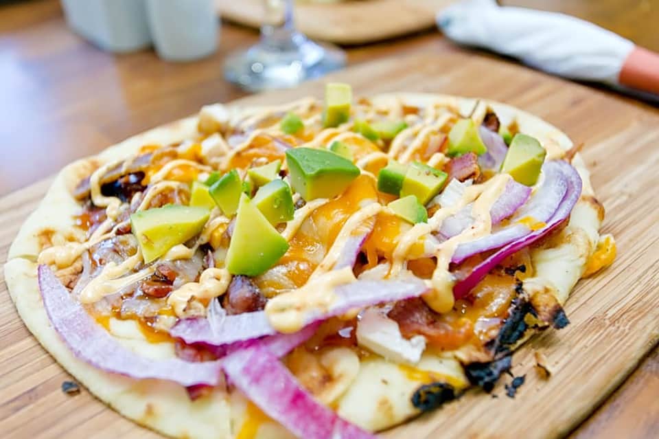 Gourmet flatbread pizza with pulled meat, purple onions, and green peppers on wooden serving board