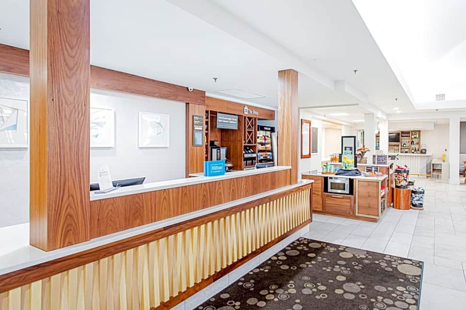 Hotel front desk with wooden paneling and check-in counter in bright, modern lobby with tiled flooring