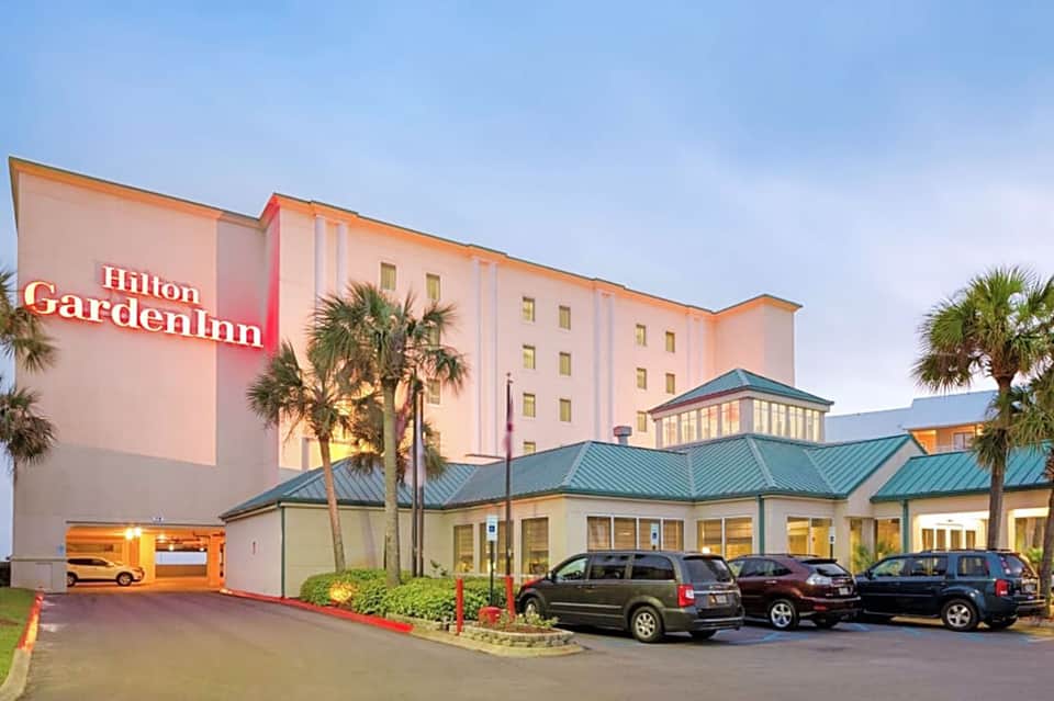 Hilton Garden Inn hotel exterior with palm trees and parked cars at dusk